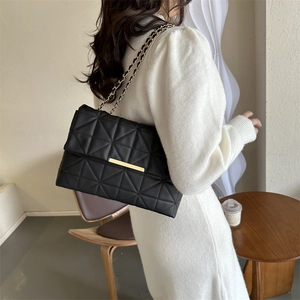 Sac bandoulière noir matelassé avec chaîne dorée porté par un mannequin en studio