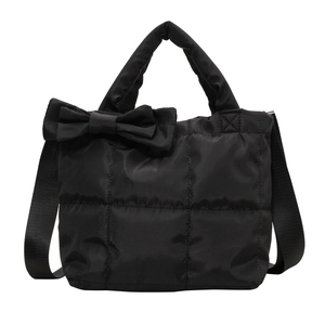 Black quilted tote bag with large bow detail and adjustable shoulder strap on white background