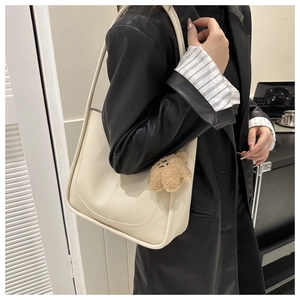 Detail view of cream white leather shoulder bag with cute plush bear charm on strap