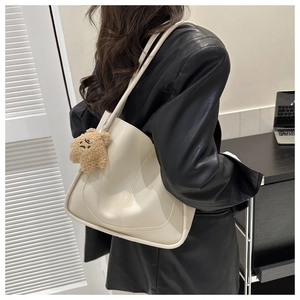 Detail of cream white tote bag with brown plush bear charm worn by a model in a blazer