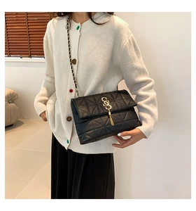Détail du sac bandoulière noir matelassé avec logo S doré, pompon et bandoulière chaîne