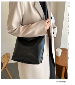 Détail d'un sac seau minimaliste en cuir noir porté par un mannequin dans un bureau