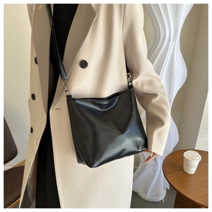 Détail du sac seau noir en cuir mat minimaliste porté par un mannequin en extérieur