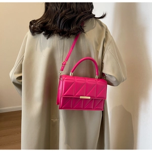 Detail of fuchsia quilted handbag with gold clasp worn by model in beige trench coat