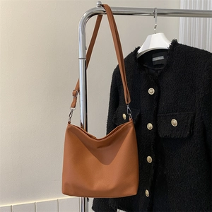 Brown lychee leather crossbody bucket bag hanging with a stylish tweed jacket