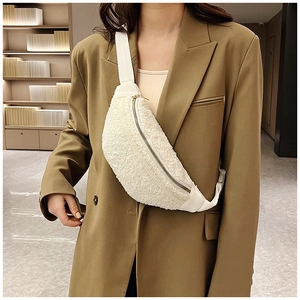 Close-up of white plush fleece crossbody bag with gold zipper worn on a brown blazer
