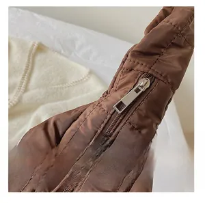 Macro detail of the smooth silver zipper and quilted fabric on a brown tote bag