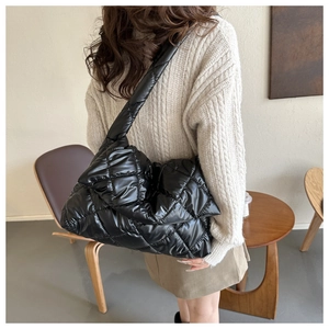 Side view of a black glossy quilted shoulder bag worn by a model in a cafe setting