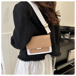 Detail of minimalist two-tone crossbody bag featuring patterned wide shoulder strap and gold hardware