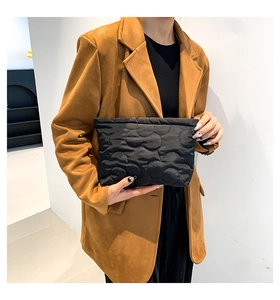 Detail van een zwarte gewatteerde clutch met golfpatroon en glanzende textuur
