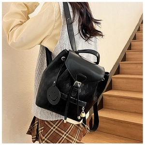 Détail du sac à dos noir avec texture matelassée et charm décoratif de visage souriant