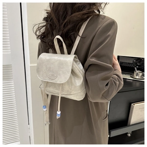 Detail of cream mini backpack showing leather texture, drawstring with beads and fashion logo