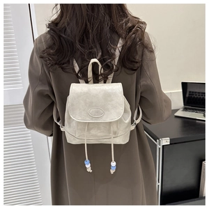 Detail of cream mini backpack with drawstring closure and decorative beads on back of model