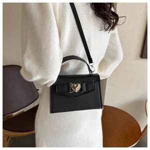 Détail du sac en cuir noir avec fermoir en cœur doré et décoration de nœud élégant