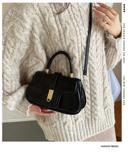 Detail of black faux leather handbag with gold metal clasp on cable knit sweater