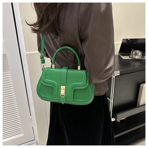 Close-up of a glossy green leather shoulder bag with a gold twist lock on a model