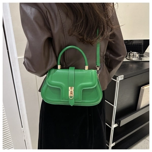 Detail of a bright green semi-circular crossbody bag with golden hardware on a model