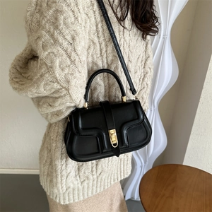 Minimalist black faux leather handbag with gold metal clasp on model in beige sweater