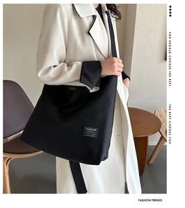 Detail view of large black canvas tote bag with adjustable shoulder strap and fashion label