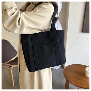 Détail du sac cabas en toile noire avec sangles renforcées et poche avant pratique