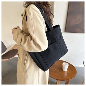 Vue détaillée du grand sac cabas en toile noire avec poche extérieure porté à l'épaule