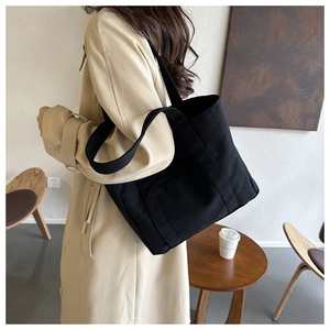 Détail d'un grand sac cabas en toile noire minimaliste porté par un mannequin en intérieur