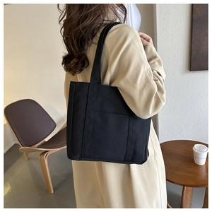 Détail d'un grand sac cabas noir en toile avec poche frontale porté par un mannequin