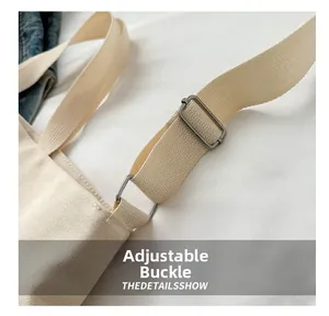 Detail of adjustable shoulder strap and metal buckle on off-white canvas tote bag