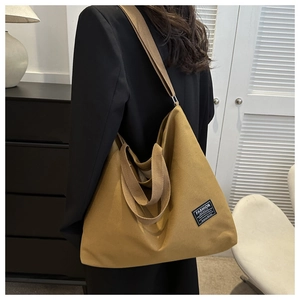 Detail of a large yellow canvas tote bag with adjustable straps and decorative logo patch