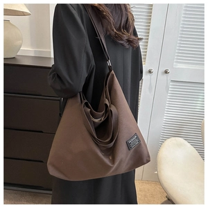 Macro detail of brown canvas tote bag featuring wide strap and fashion logo patch