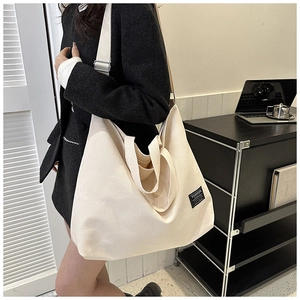 Detail of cream canvas tote bag with fashion label and shoulder strap on model