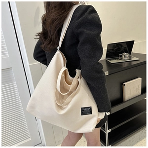 Detail of a large off-white canvas tote bag worn over the shoulder in an office setting