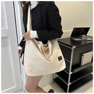 Close-up of cream canvas tote bag showing fashion label, dual handles and wide strap