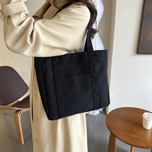 Sac fourre-tout noir minimaliste en toile avec poche portée sur un trench-coat beige