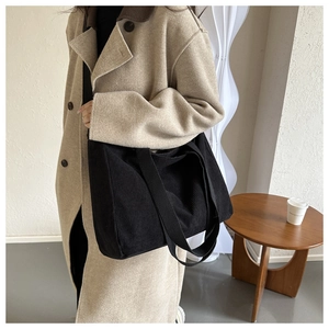 Detail shot of black corduroy tote bag texture worn with a beige coat for a stylish look
