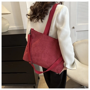 Detail of burgundy corduroy hobo bag with dual straps worn by a model in a home setting
