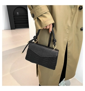 Dettaglio borsa nera goffrata lucertola con chiusura a anello dorato e trench color kaki