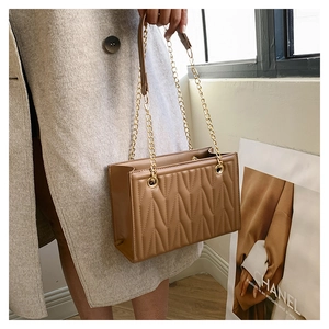 Detail of tan quilted faux leather shoulder bag with golden chain strap on a model