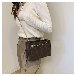 Close-up of deep brown wavy quilted crossbody bag with gold chain strap on model