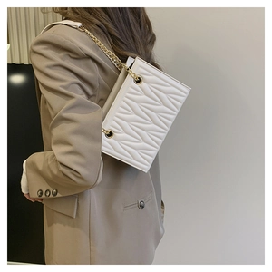 Close-up of a white quilted crossbody bag with gold chain strap on a khaki blazer