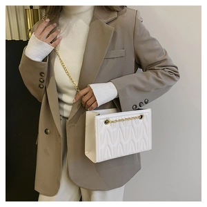 Detail view of white quilted faux leather crossbody bag with golden chain strap on model
