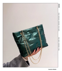 Detail of dark green quilted tote bag with golden chain straps and silky metallic texture