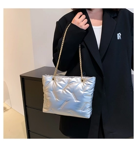 Detail of silver puffer tote bag with quilted texture and gold chain strap on model