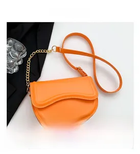 Detail of orange leather saddle bag featuring wavy flap edges and gold chain strap