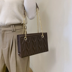 Dark brown quilted chain shoulder bag with V-shaped stitching shown on a model