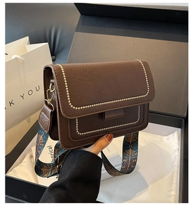 Detail of dark brown leather crossbody bag with gold rivets and woven shoulder strap