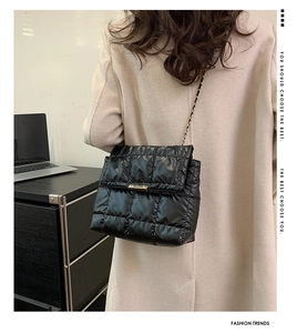 Detail of black quilted shoulder bag with gold chain strap worn over a beige coat