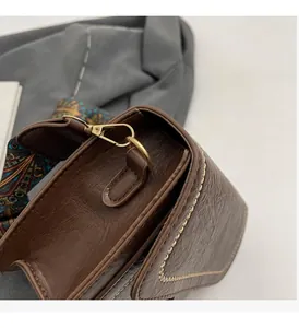 Detail of dark brown leather crossbody bag with gold hardware and ethnic woven strap