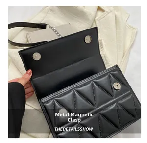 Detail view of the silver magnetic snap closures on a black quilted shoulder bag