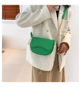 Detail of bright green crossbody bag with wavy flap design and gold chain strap